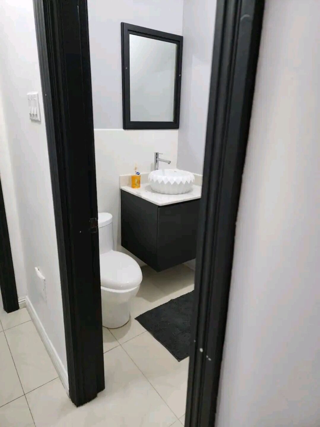 Ein Badezimmer mit Toilette, Waschbecken mit Spiegel darüber und schwarzem Teppichboden.