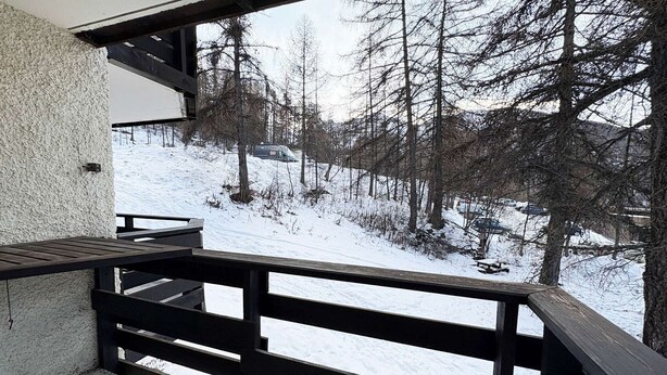 A balcony with a view of a snowy landscape and trees.