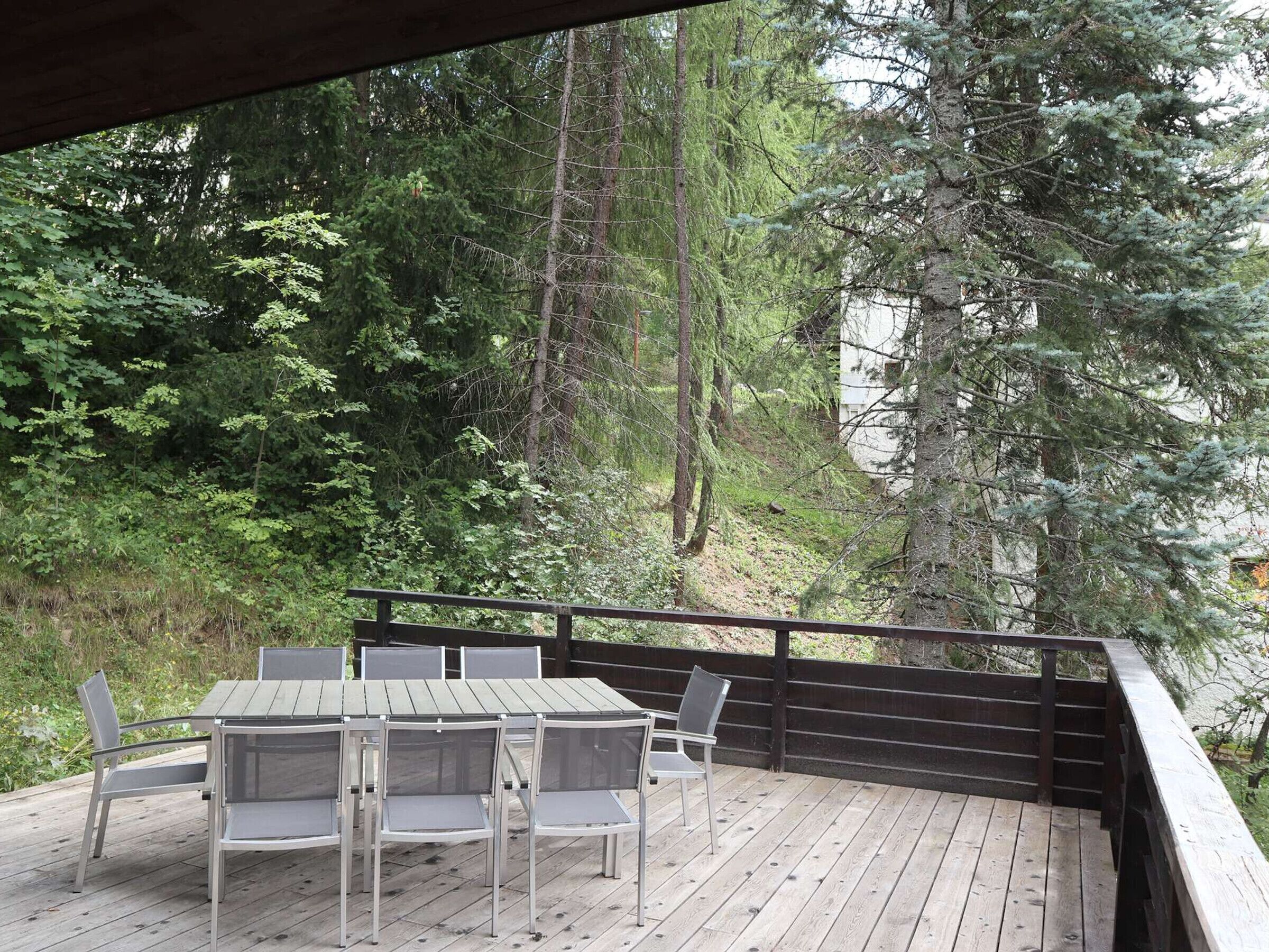 An outdoor deck with a table and chairs, surrounded by dense forest and tall trees.