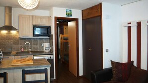 A compact kitchen with a microwave, coffee maker, and wooden cabinets. There is a dining area with a table and chairs, and a sofa in the living room. - Bright studio for 4 in the heart of the resort with balcony (Les Orres)