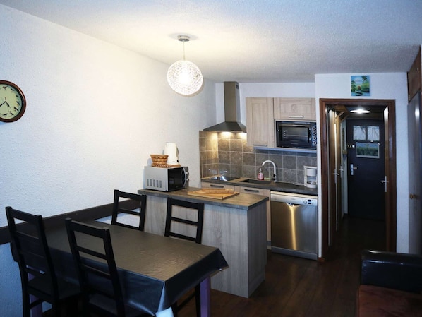 A compact kitchen with a dining area, featuring a microwave, stove, sink, and a clock on the wall.