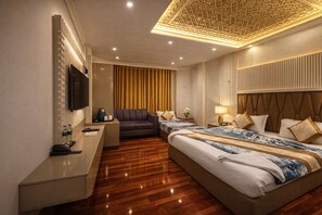 Quarto de hotel com uma cama grande, um sofá, uma televisão, uma mesa e teto decorativo.