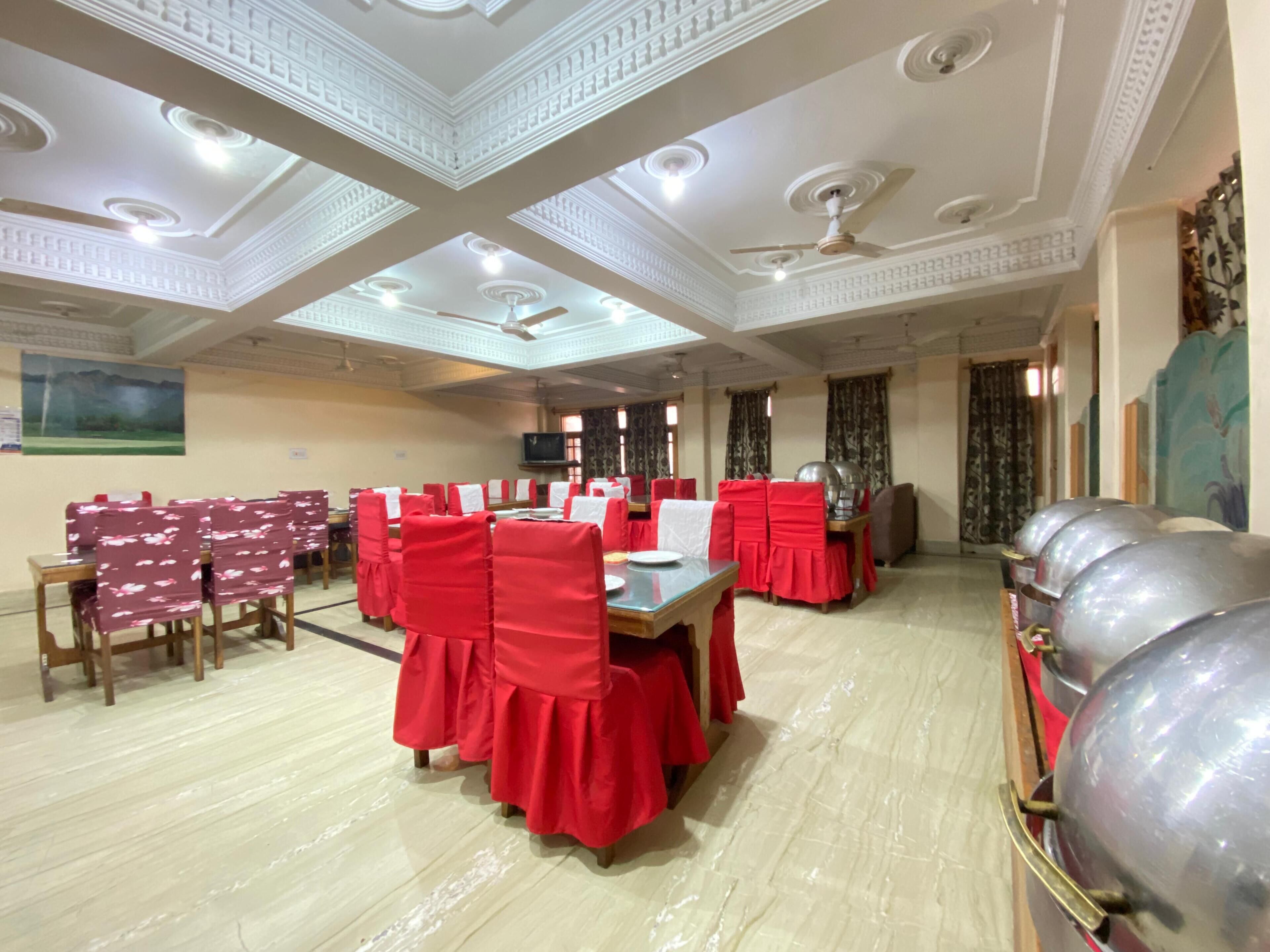 A banquet hall with red-covered tables and chairs, a ceiling with recessed lighting, and a large decorative wall piece.