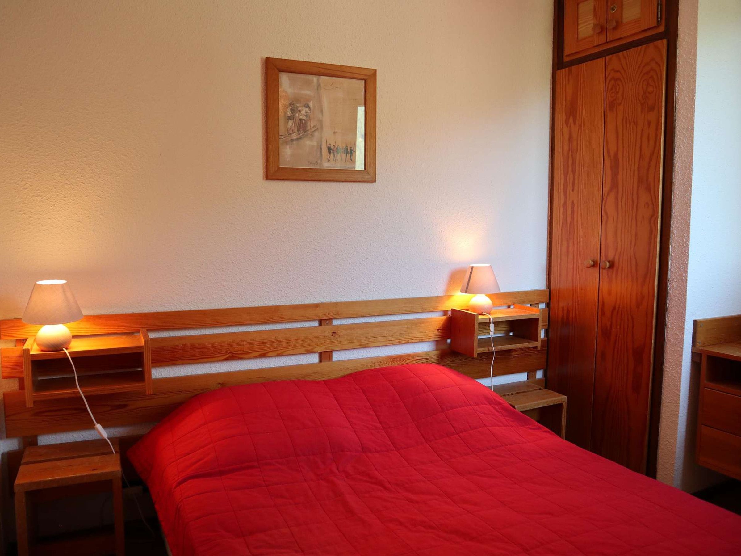 A bedroom with a wooden bed, two bedside tables with lamps, a wooden wardrobe, and a framed picture on the wall.