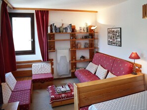 A cozy room with a red sofa, two matching armchairs, a wooden bookshelf, and a window with red curtains.