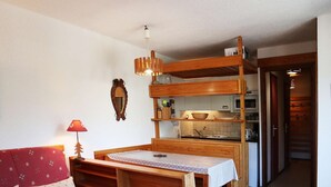 A cozy room with a wooden bunk bed, a small kitchenette, and a red sofa.