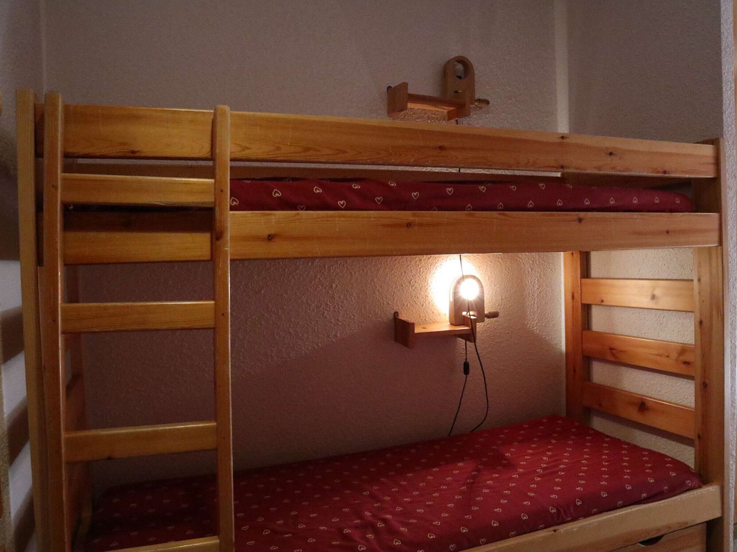 Ein Etagenbett mit einer Leiter, ein Nachttisch mit Lampe und eine gemusterte Bettdecke.