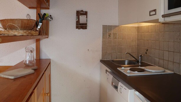 A compact kitchen with wooden shelves, a microwave, and a tiled backsplash.