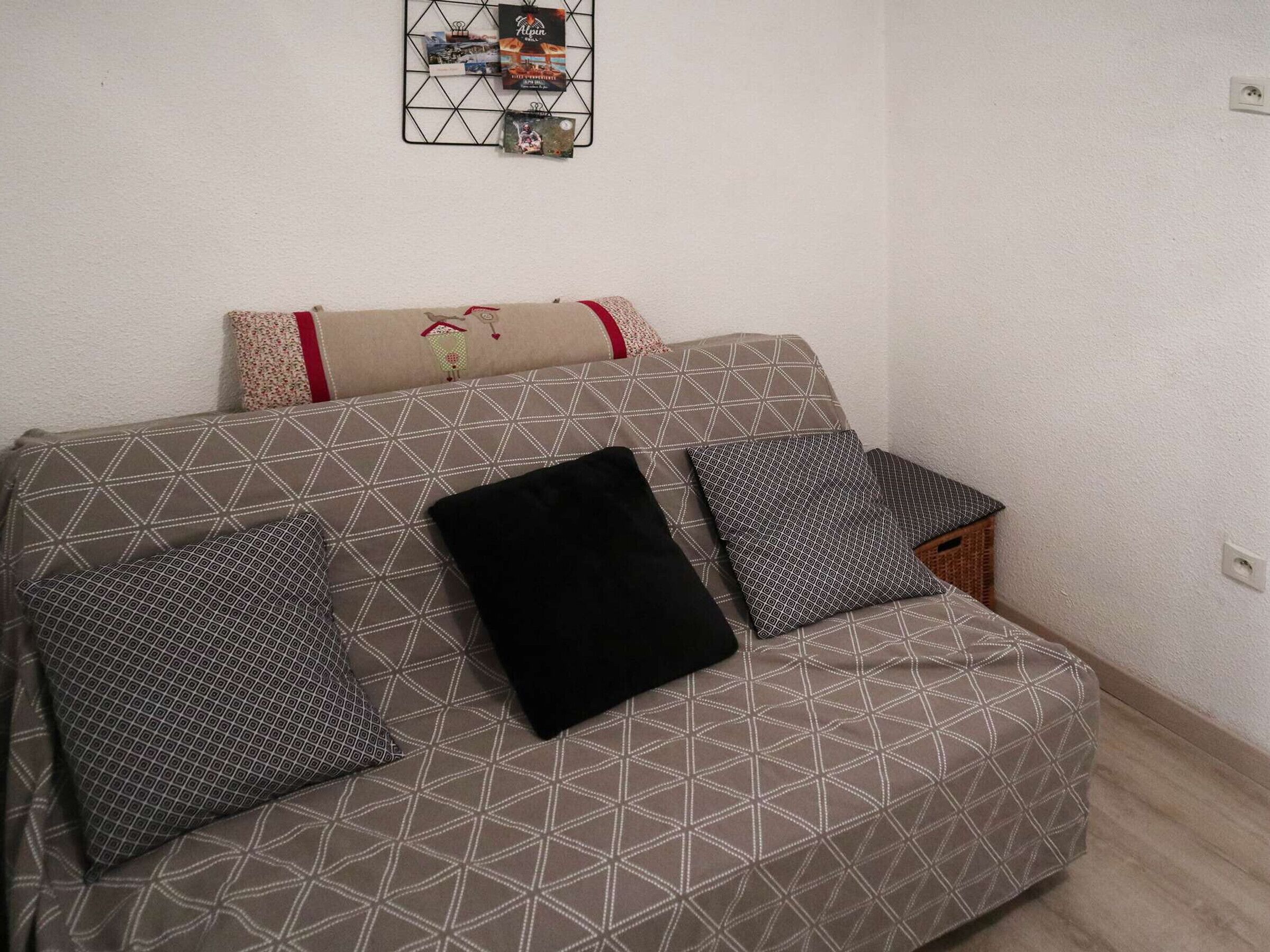 A modern living room with a geometric-patterned sofa, a black throw pillow, and a decorative wall hanging.