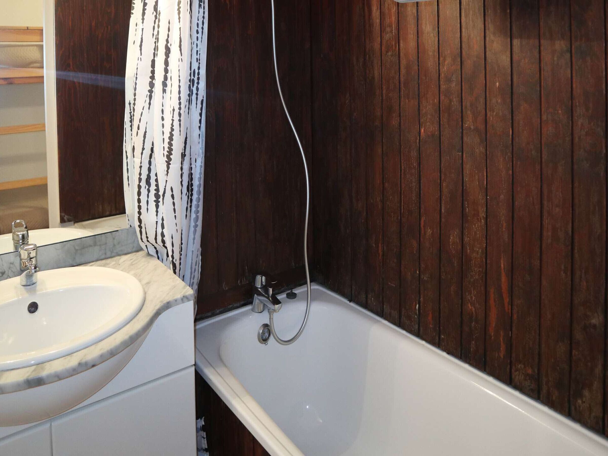 Een badkamer met een witte wastafel, een bad en een houten wand.