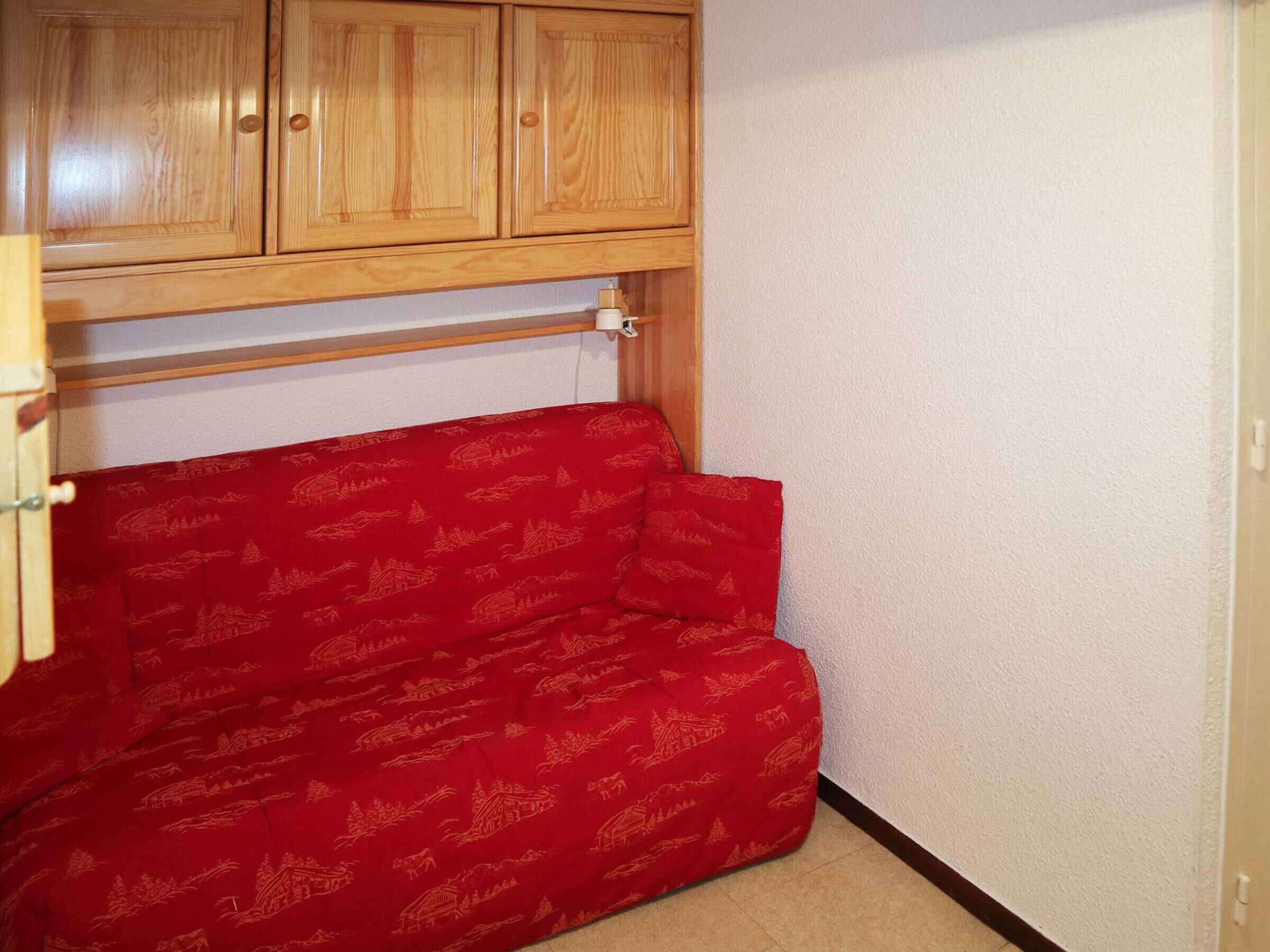 Une pièce de taille modeste, avec un canapé rouge, des meubles en bois et un mur blanc.