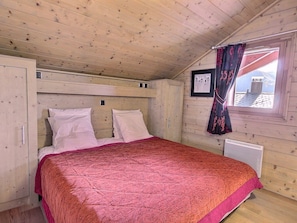 Une chambre confortable avec un plafond et des murs en bois, un lit avec des oreillers blancs, une couverture rouge et une fenêtre avec des rideaux.