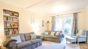 A living room with a sofa, two armchairs, a bookshelf, and a window with curtains. - The Old Lace Shop (Seaton)