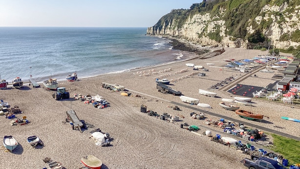 A beach with boats, a tractor, and a rocky cliff. - The Old Lace Shop (Seaton)