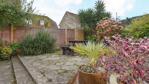 A garden with a stone pathway, a wooden bench, and various potted plants. - The Old Lace Shop (Seaton)