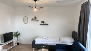 Ein modernes Wohnzimmer mit einer Couch, einem Fernseher, einem kleinen Tisch und einer Deckenleuchte.
