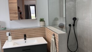 Ein modernes Badezimmer mit einer Duschkabine aus Glas, einem Holzlagerfeld und einem weißen Waschbecken sowie einem Spiegel über dem Waschtisch.