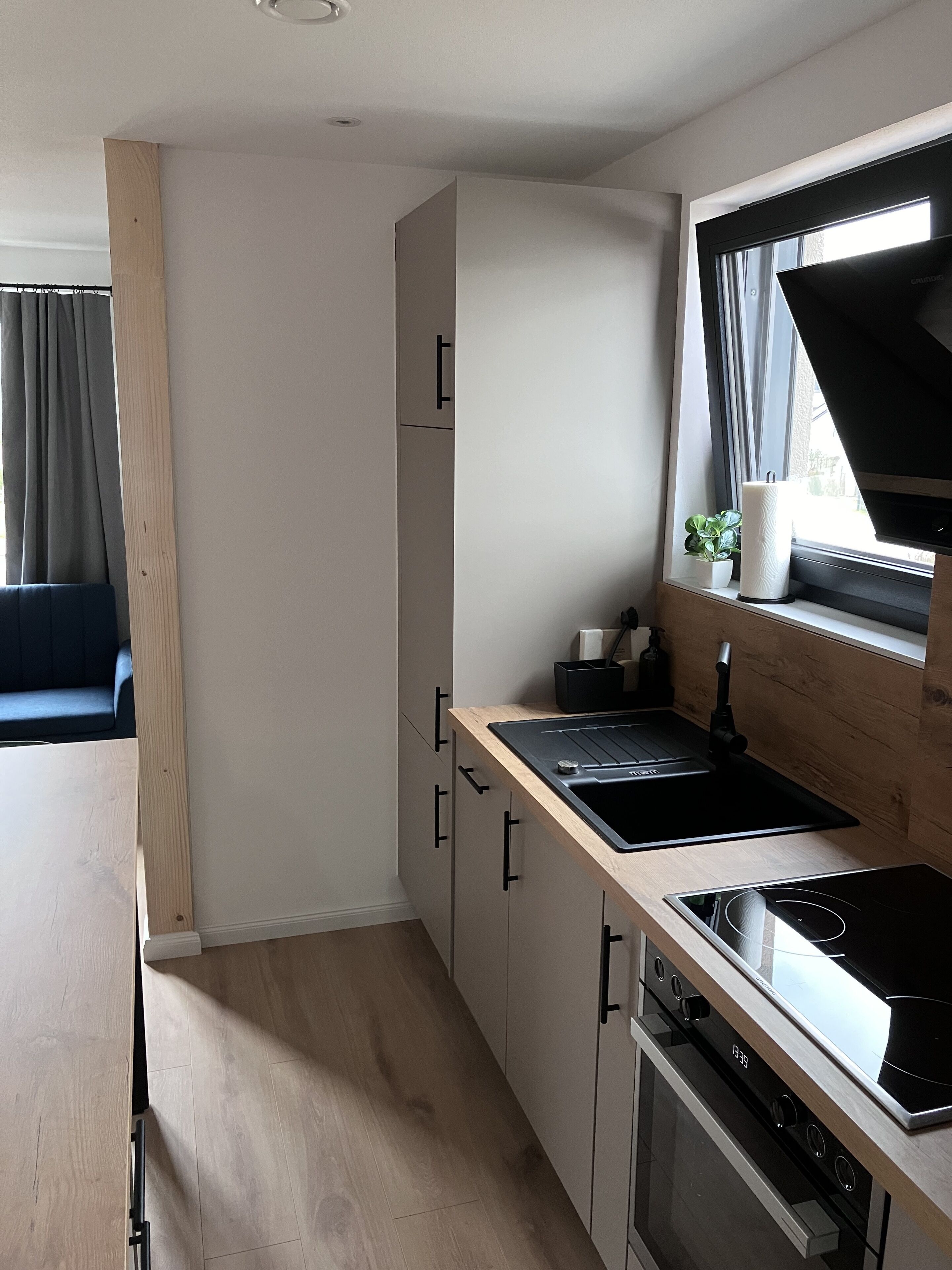 A modern kitchen with a wooden countertop, black appliances, and a window with curtains.