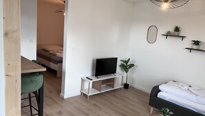 Ein modernes Wohnzimmer mit Fernseher, Sofa, einem kleinen Tisch und einem Essbereich mit einem Stuhl.