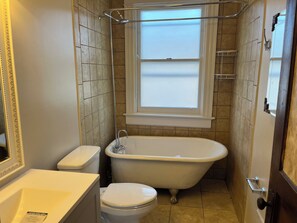 A bathroom with a bathtub, toilet, and a window.