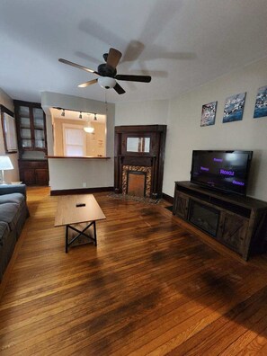 A living room with a fireplace, a television, and a ceiling fan. - Cleneay #2, Private 3 Bed near Xavier & Downton (Norwood)