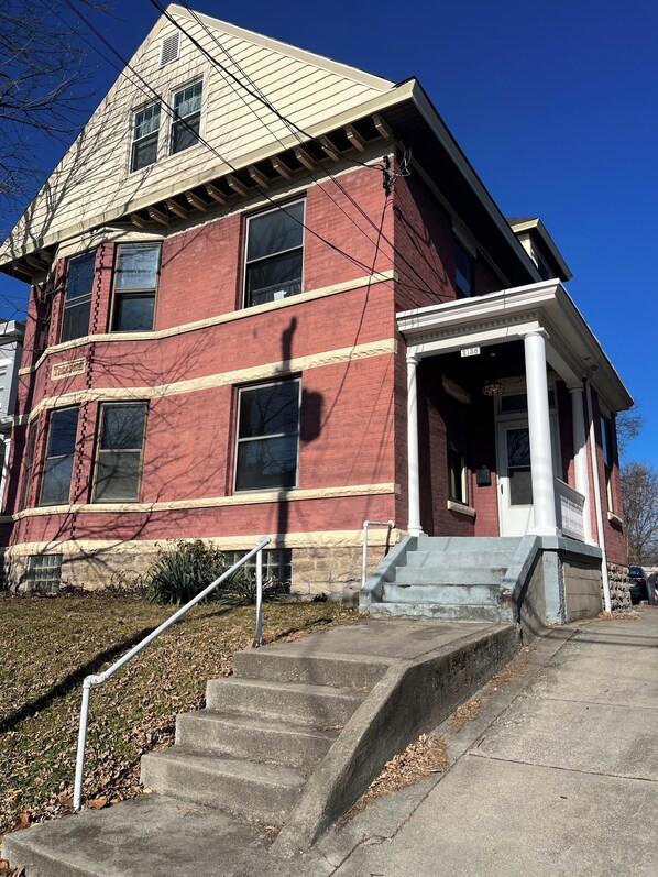 A two-story building with a red brick facade, a white trim, and a set of stairs leading to a front door.
