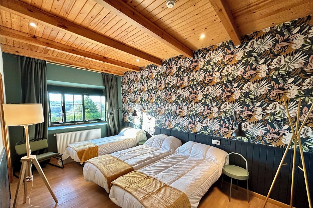 A room with two beds, a window with curtains, a radiator, a lamp, and a wall with a floral pattern.