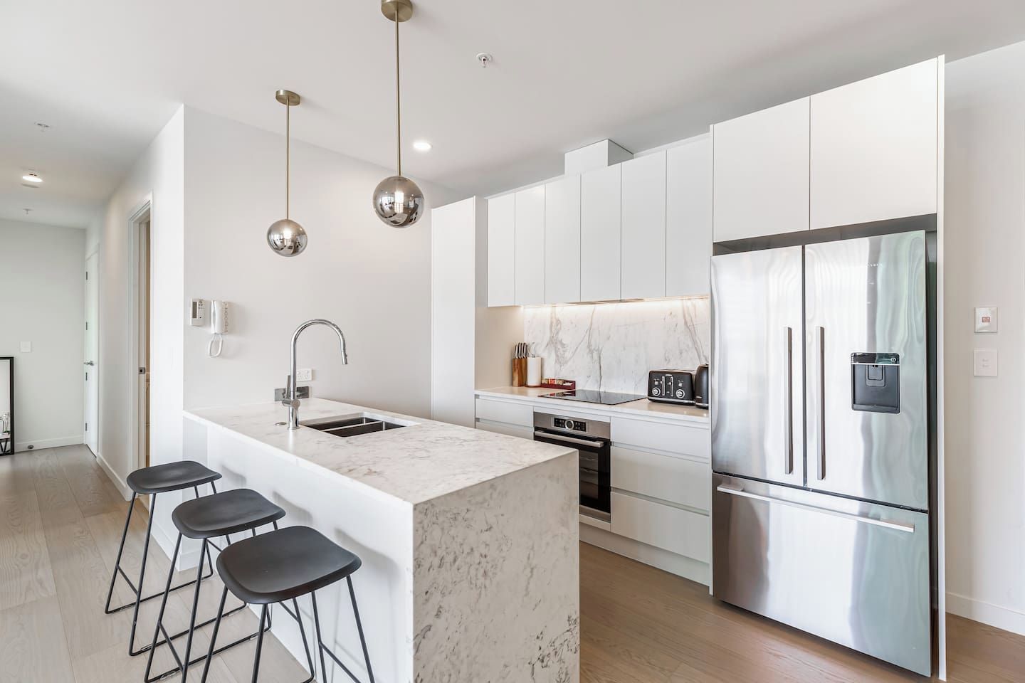 A modern kitchen with a central island, stainless steel appliances, and a marble countertop.