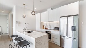 Une cuisine moderne avec des meubles blancs, un îlot en marbre, des appareils électroménagers en acier inoxydable et des luminaires suspendus.