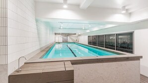 Une piscine intérieure moderne avec des parois en verre transparent, un sol carrelé et une zone de pont en bois.