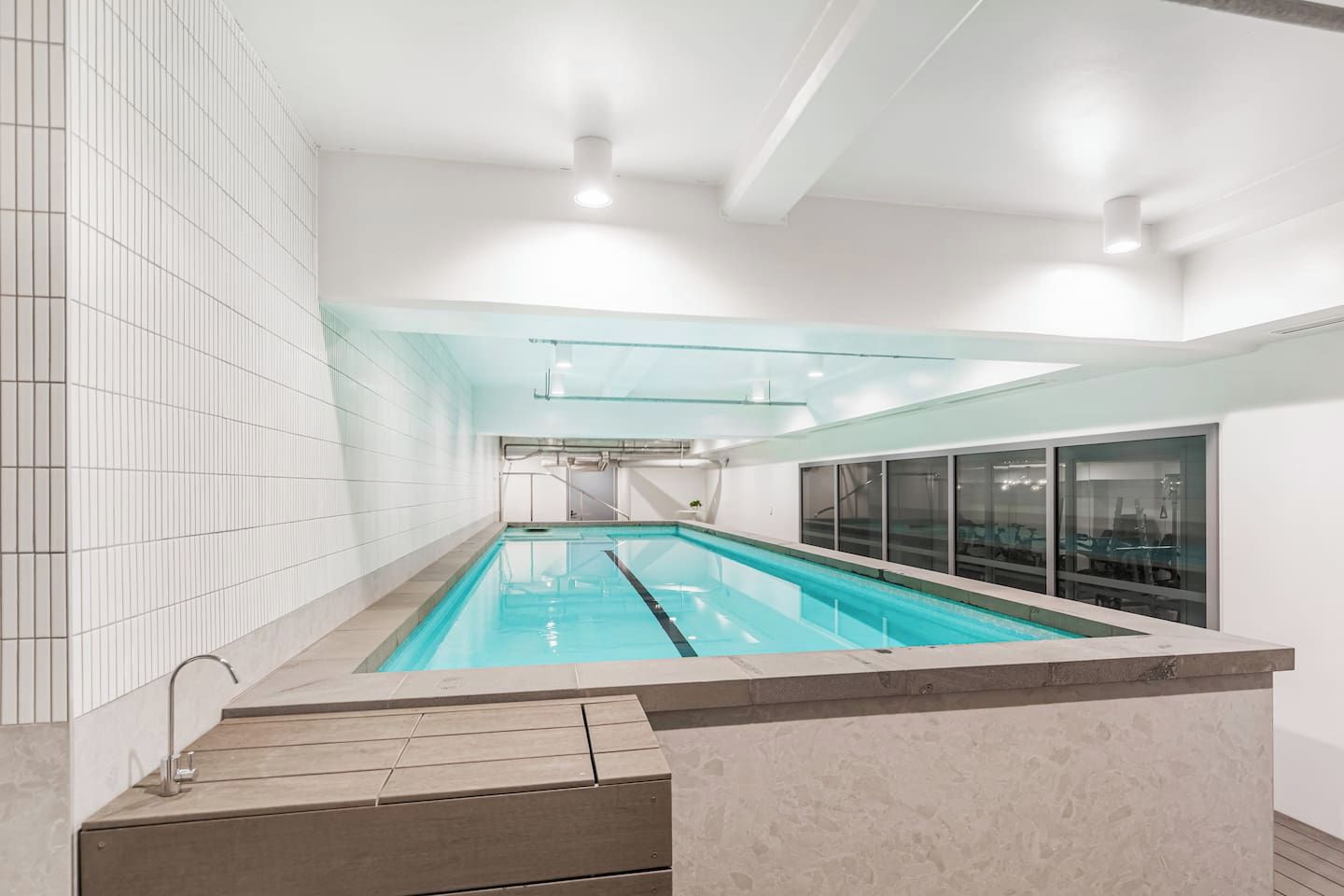 Une piscine avec des couloirs bien délimités, un mur en verre d’un côté et un mur carrelé de l’autre.