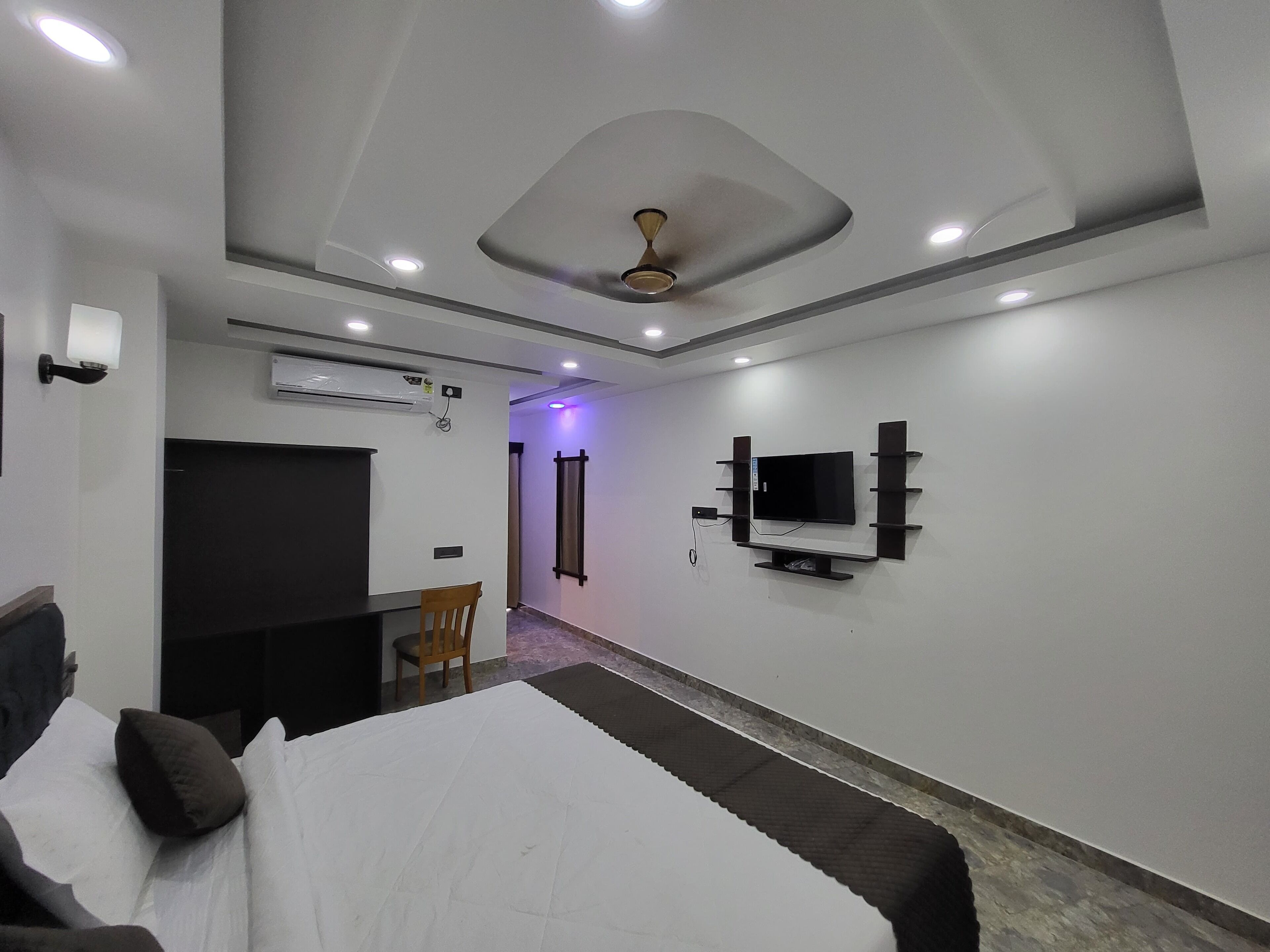 A modern bedroom with a bed, a TV mounted on the wall, and an air conditioning unit.