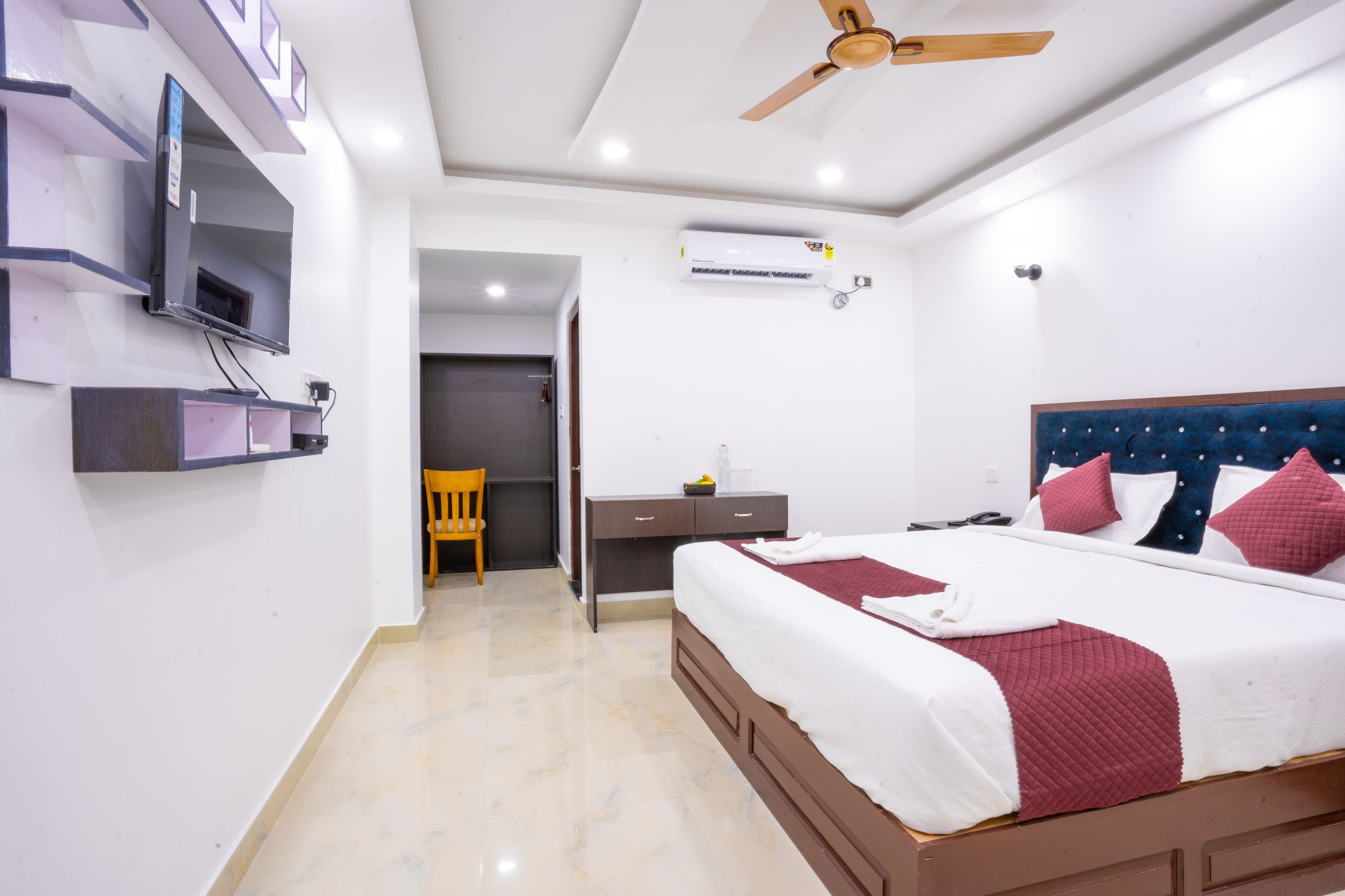 A hotel room with a bed, a desk, a chair, a television, and an air conditioning unit.