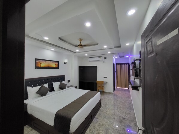 Una habitación de hotel moderna con una cama grande, ventilador de techo, iluminación empotrada, aire acondicionado y vista al pasillo.