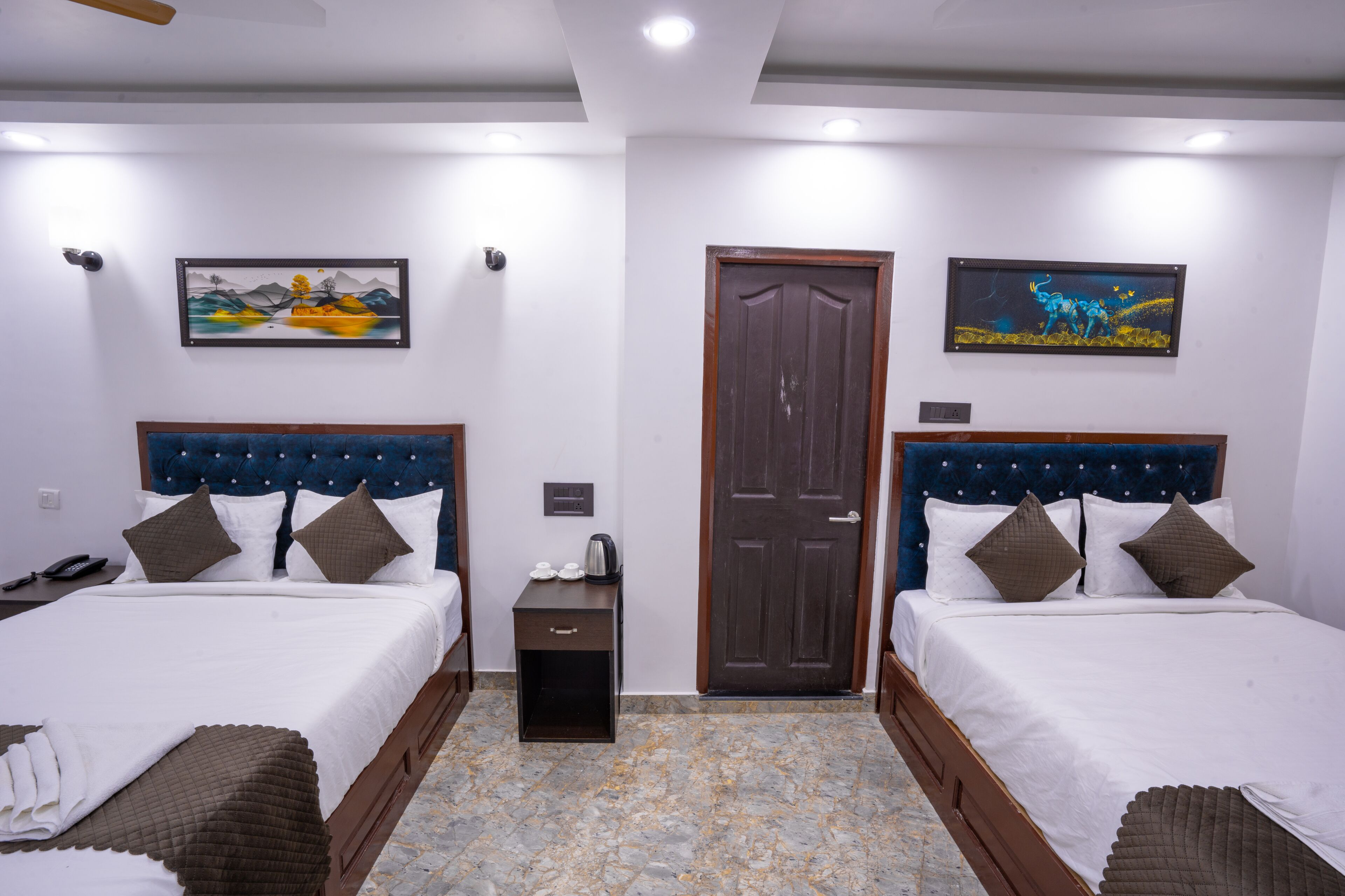 A hotel room with two beds, a small table, a nightstand, and a door.