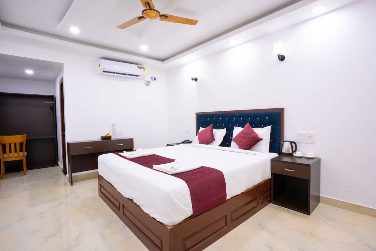 Una habitación de hotel con una cama, un escritorio, una silla, una mesita de noche, un aire acondicionado y un ventilador de techo.