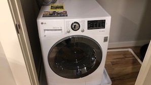 A compact, white LG Direct Drive front-loading washing machine with a digital display, situated in a small room with wooden flooring and a white door.