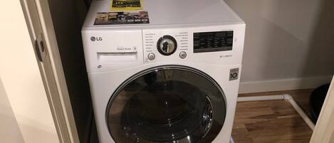 A compact, white LG Direct Drive front-loading washing machine with a digital display, situated in a small room with wooden flooring and a white door.