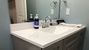 A bathroom with a white sink, two bottles of hand soap, a towel, and a toilet paper holder.