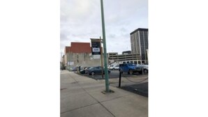 A street view with a parking lot, a building with a red roof, and a blue car parked.