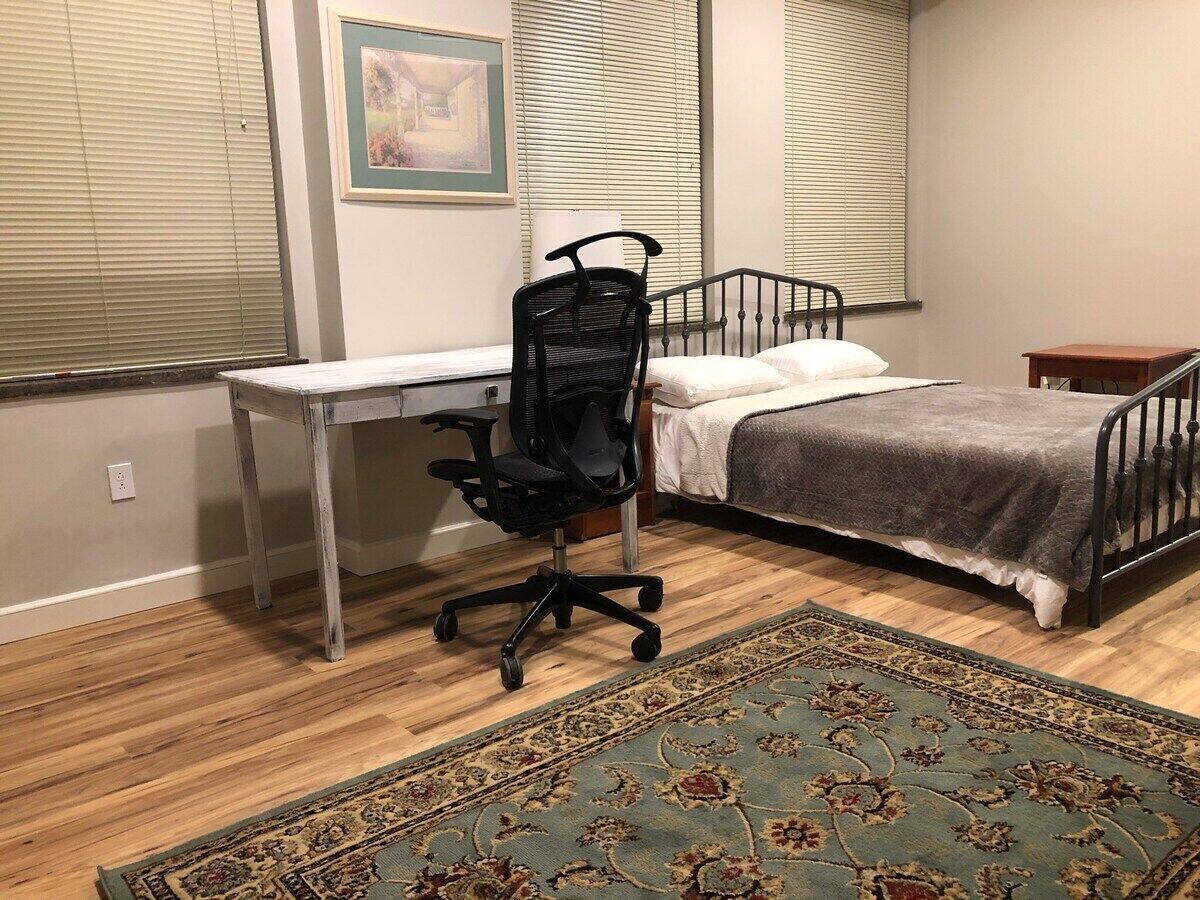 A bedroom with a bed, a desk, a chair, and a rug.