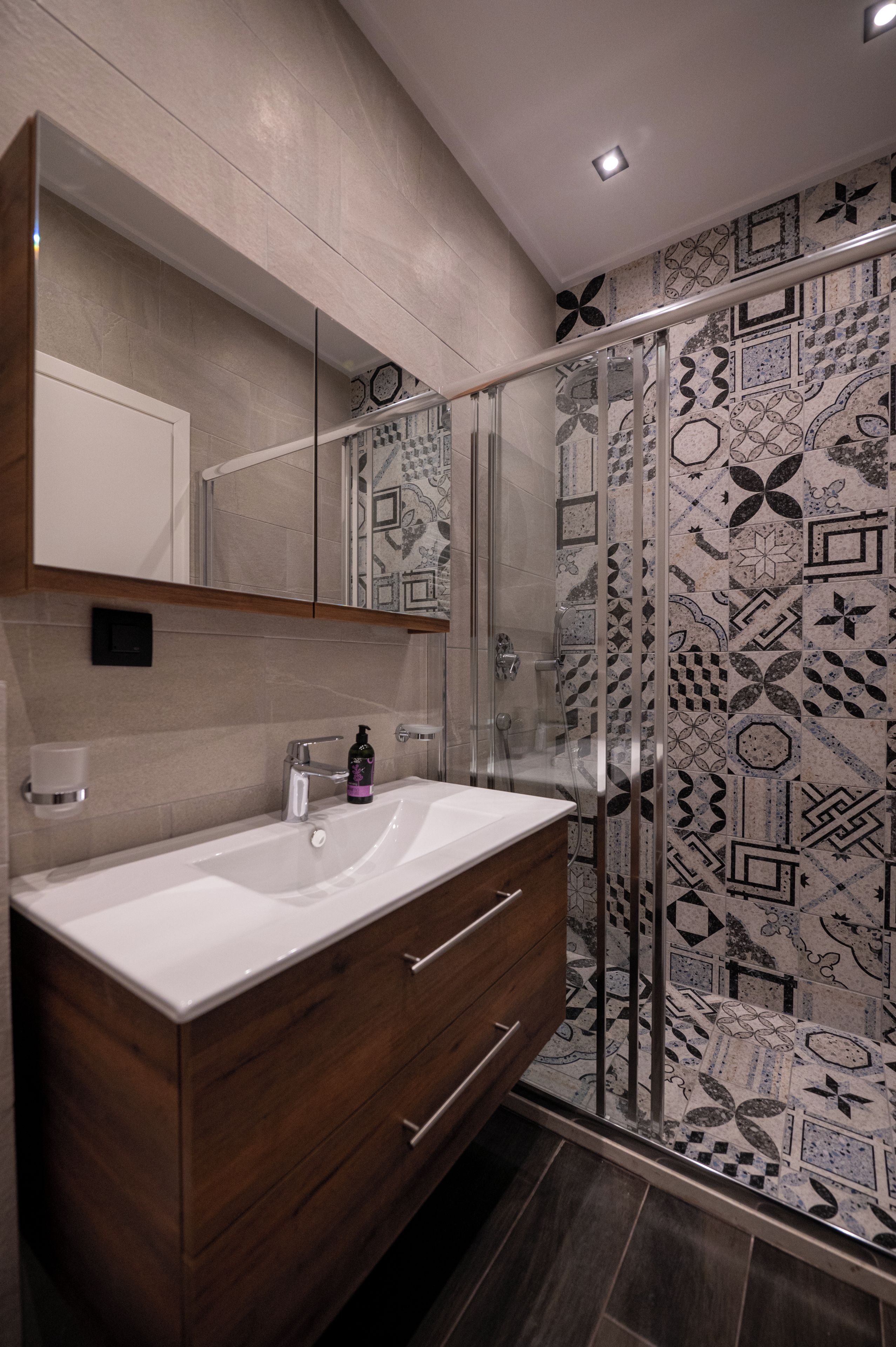 Une salle de bain moderne avec un meuble-lavabo en bois, une cabine de douche en verre et des murs recouverts de carreaux à motifs.