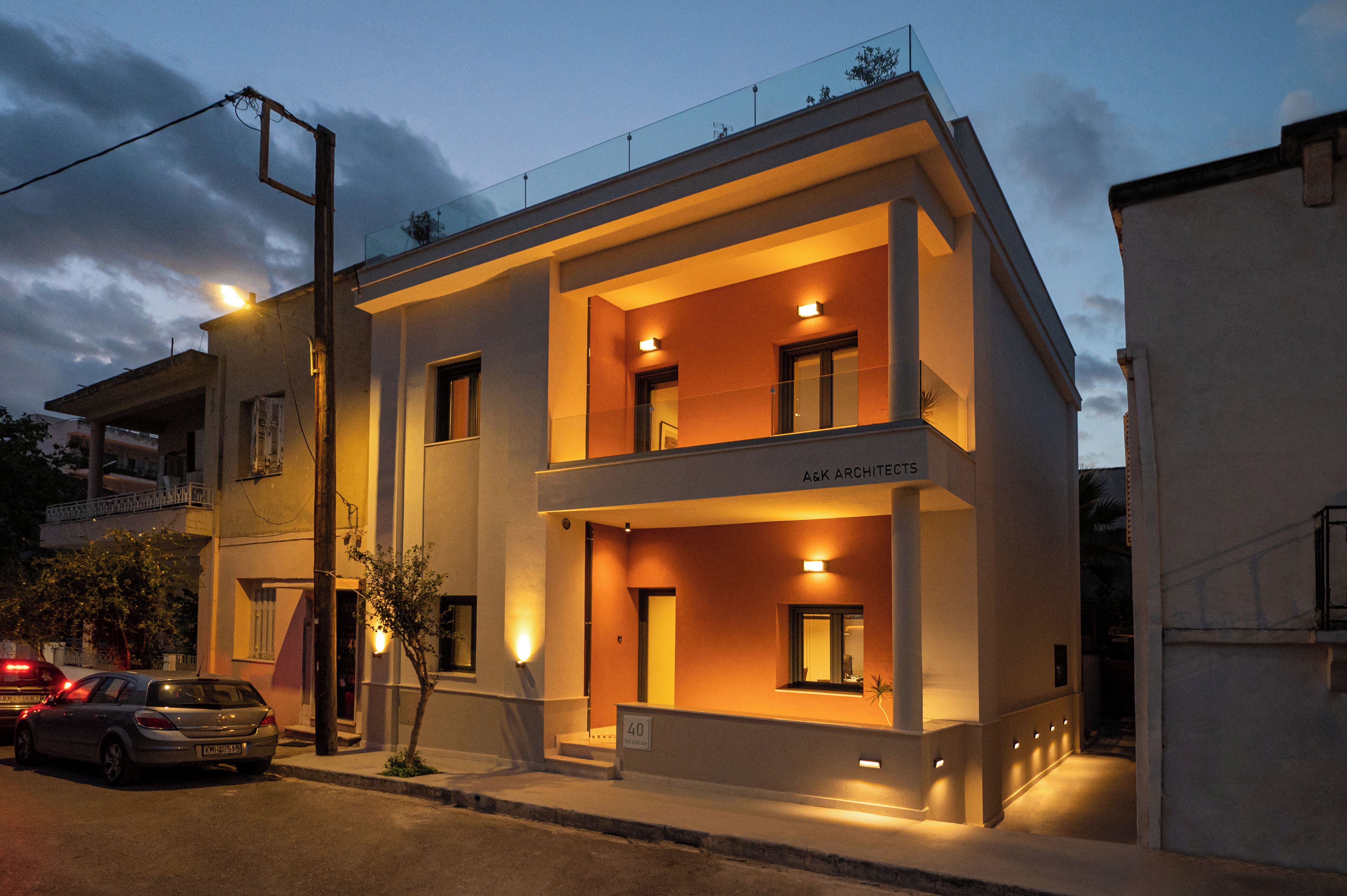 A modern two-story building with a balcony, a sign reading 'Ask Architects,' and a parked car.