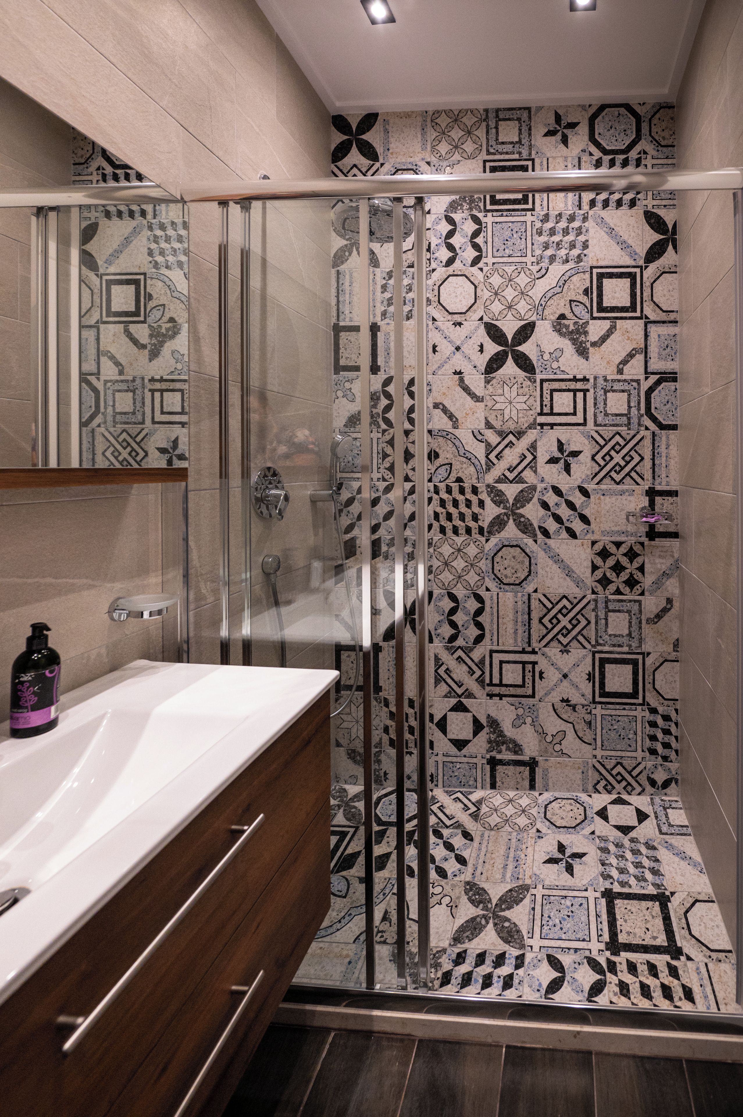 Un bagno con box doccia in vetro, lavandino bianco e mobile contenitore in legno.