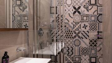 Un bagno con box doccia in vetro, lavandino bianco e mobile contenitore in legno.