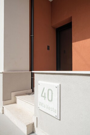 L’entrée d’un immeuble, avec une plaque indiquant « 40, villa Vesta », des marches menant à l’entrée et une porte dotée d’un cadre noir.