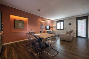 A modern living room with a wooden dining table, clear chairs, a sofa, and a TV. - Villa Vesta - Kalamata Mediterranean Suites & Villas (Kalamata)