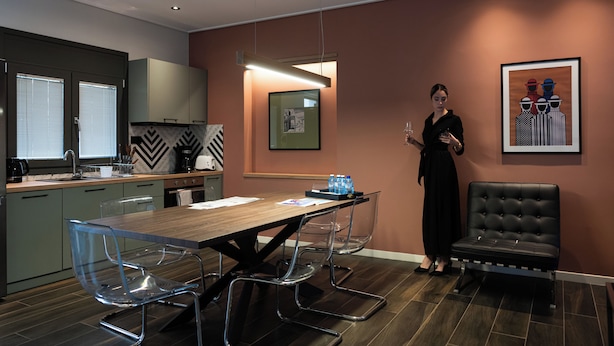 A modern kitchen with a dining area, featuring a wooden table, clear chairs, and a black leather sofa. - Villa Vesta - Kalamata Mediterranean Suites & Villas (Kalamata)