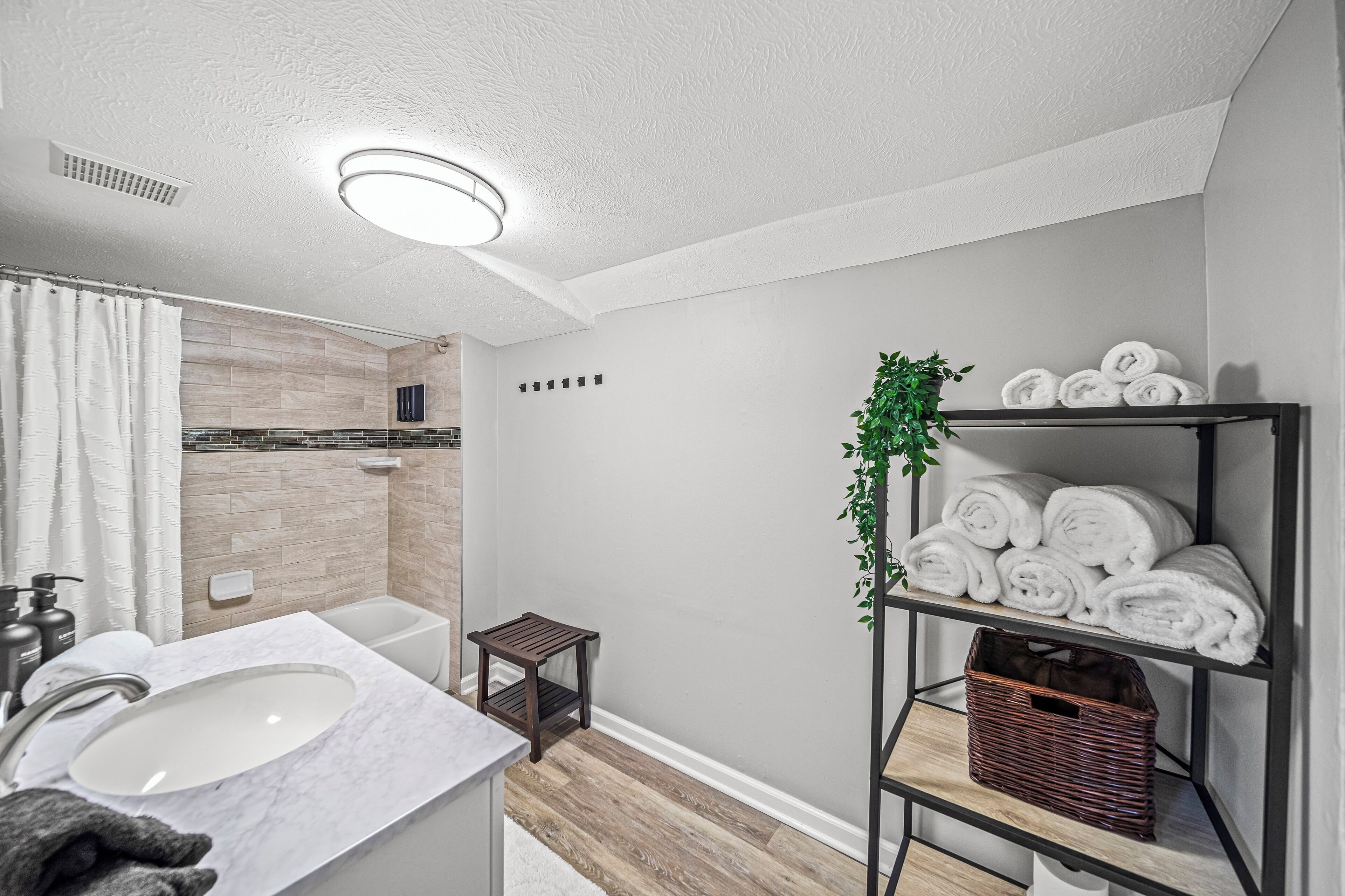 Een moderne badkamer met een wit wastafelmeubel, een klein houten krukje, een plank met handdoeken en een plant.
