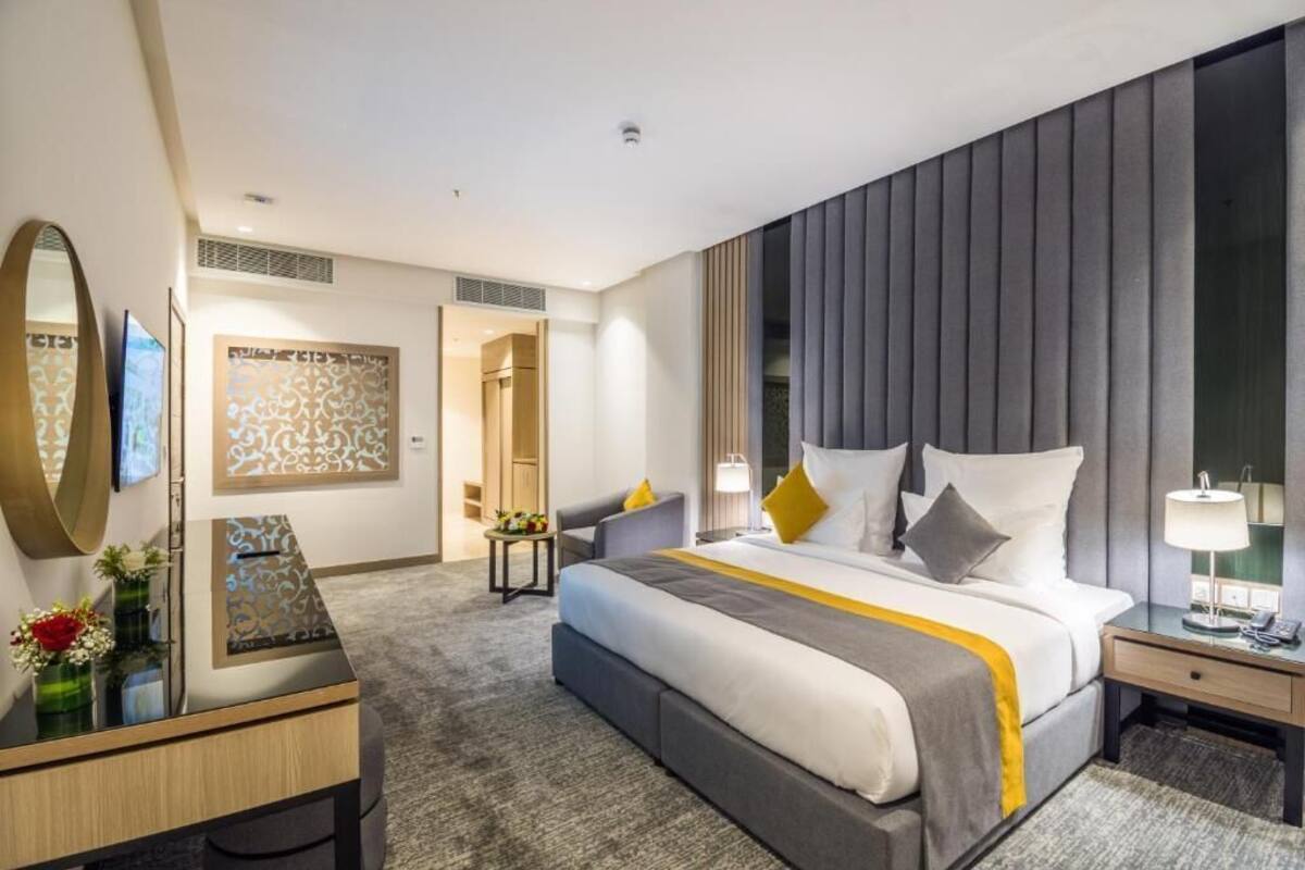 A modern hotel room with a large bed, a desk, a chair, and a TV.
